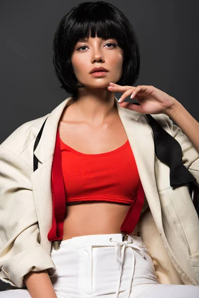 Attractive young woman in beige jacket and untied bowtie over red crop top looking at camera isolated on grey — Stock Photo