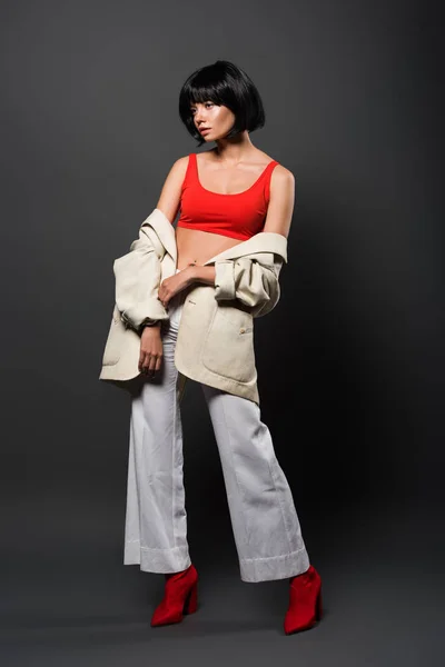 Hermosa mujer joven con el pelo enmohecido en top de la cosecha roja, botones de campana y chaqueta en gris - foto de stock