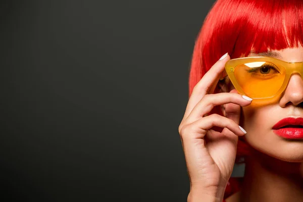 Обрезанный снимок красивой молодой женщины с рыжими волосами и винтажными желтыми очками, смотрящей на камеру, изолированную на сером — стоковое фото