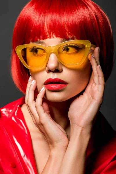 Close-up portrait of beautiful young woman in red latex jacket and vintage yellow sunglasses isolated on grey — Stock Photo
