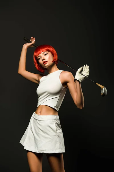 Sporty young woman in sportswear posing with golf club and looking at camera isolated on grey — Stock Photo