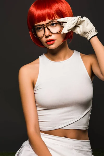 Séduisante jeune femme avec bob rouge coupé en gant de golf et des lunettes élégantes regardant loin isolé sur gris — Photo de stock