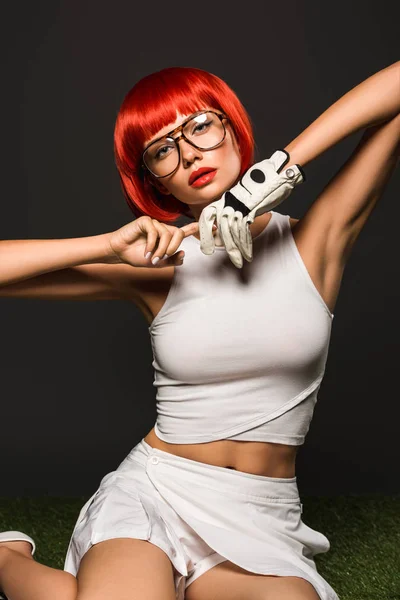 Seductive young woman with red bob cut in golf glove and stylish eyeglasses looking at camera on grey — Stock Photo