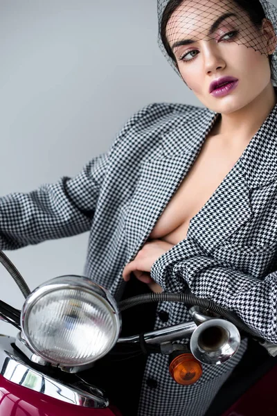 Atraente mulher sedutora em jaqueta retro e véu líquido posando em scooter clássico, isolado em cinza — Fotografia de Stock