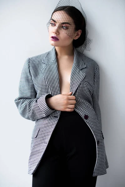 Fashionable half naked woman posing in retro jacket and net veil, on grey — Stock Photo