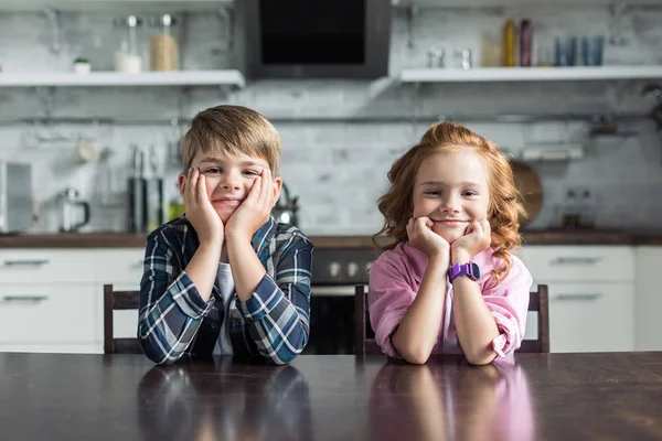 Sorridente fratellino e sorella seduti in cucina insieme e guardando la fotocamera — Foto stock