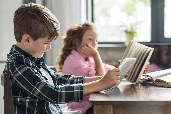 Petit garçon utilisant tablette tandis que sa soeur lecture livre — Photo de stock