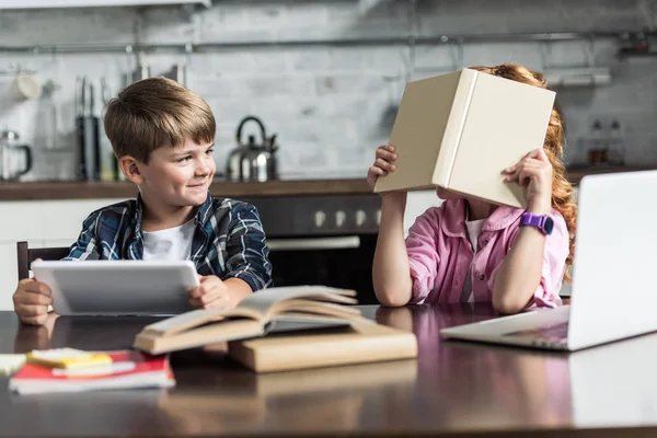 Hermano pequeño y hermana jugando durante la tarea en la cocina - foto de stock