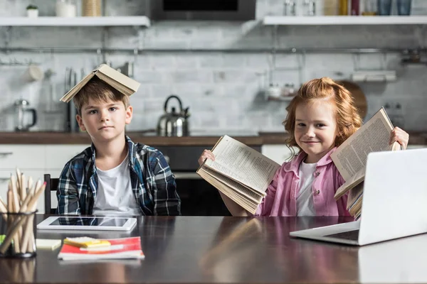 Crianças adoráveis com muitos livros olhando para a câmera na cozinha — Fotografia de Stock