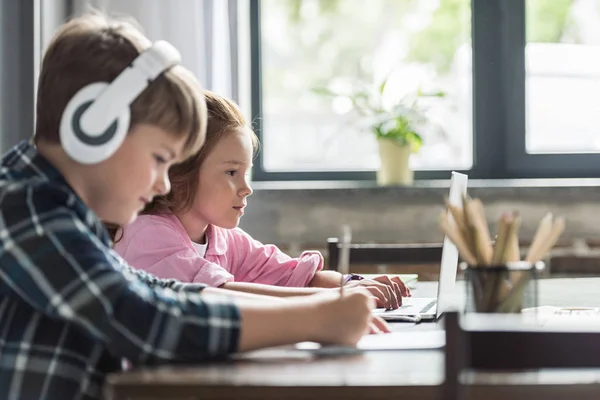 Side view of cute little schoolboy drawing with color pencils while his sister using laptop — Stock Photo