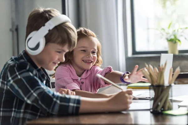 Vue de côté du petit écolier dessinant tandis que sa sœur souriante essayant d'atteindre des crayons — Photo de stock