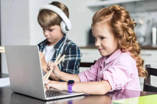 Hermano pequeño y hermana haciendo la tarea y el uso de ordenador portátil - foto de stock