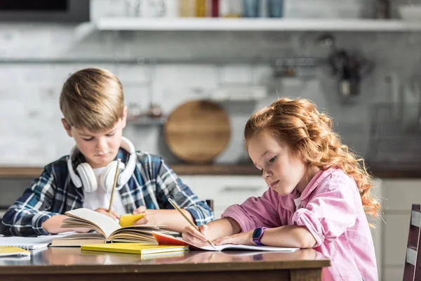 Niños pequeños concentrados haciendo tareas juntos en la cocina - foto de stock