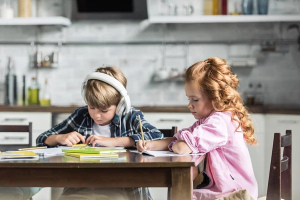 Сосредоточенные маленькие дети делают домашнее задание вместе на кухне — стоковое фото