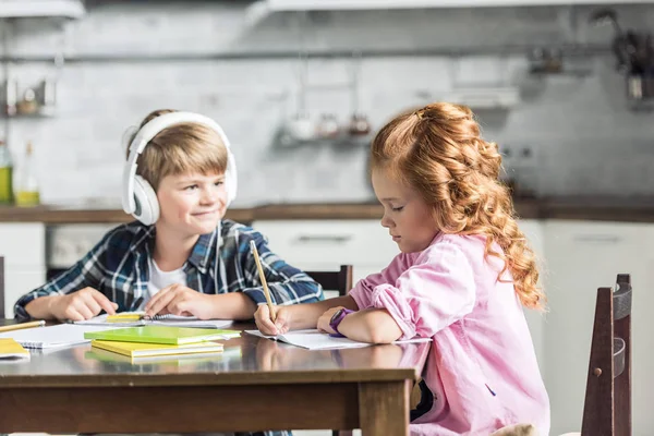 Kleines Schulmädchen macht Hausaufgaben, während ihr Bruder sie ansieht — Stockfoto