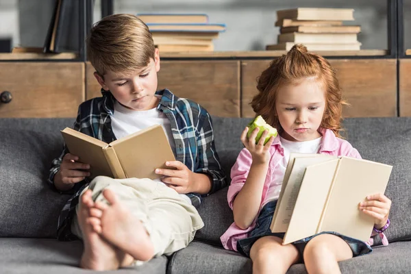 Concentrated little brother and sister reading books on couch at home — Stock Photo