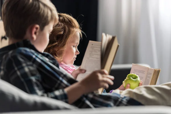 Irmãozinho e irmã lendo livros no sofá em casa — Fotografia de Stock