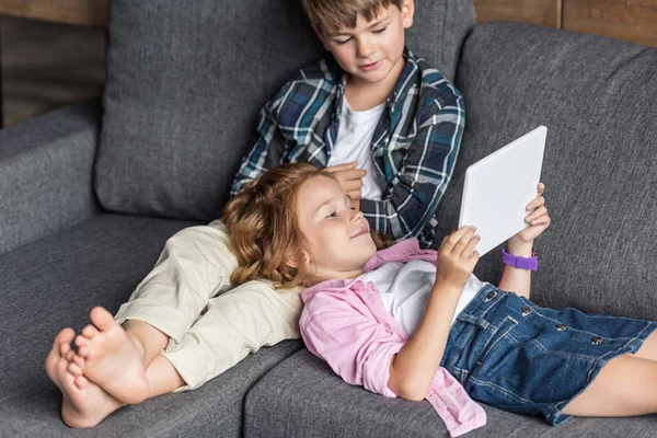 Adorable little brother and sister using tablet together while relaxing on couch — Stock Photo