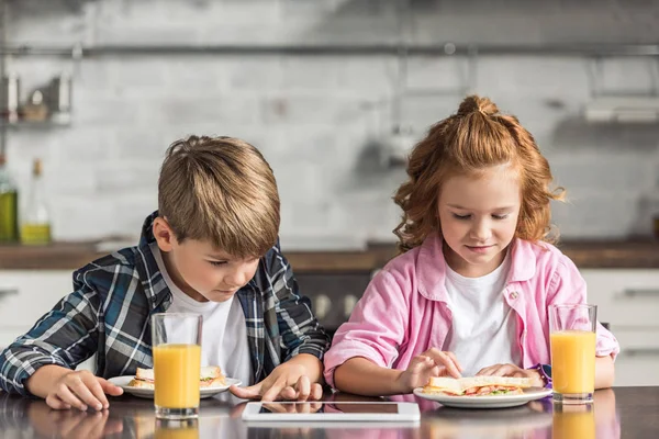 Младший брат и сестра с помощью планшета во время завтрака на кухне — стоковое фото