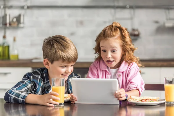 Surprised little brother and sister using tablet during breakfast — Stock Photo