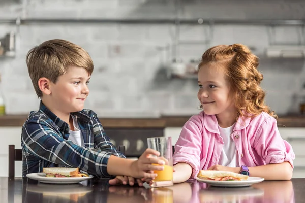 Маленький брат і сестра досягають склянки апельсинового соку під час сніданку і дивляться один на одного — стокове фото