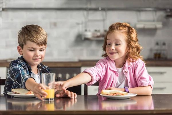 Hermano pequeño y hermana que buscan un vaso de jugo de naranja durante el desayuno - foto de stock