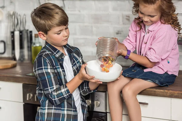 Little brother and sister pouring macaroni into bowl from jar — Stock Photo