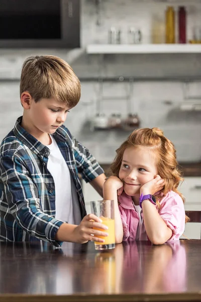 Adorabile fratellino che dà un bicchiere di succo d'arancia alla sorridente sorella — Foto stock