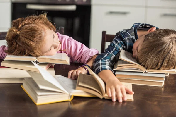 Erschöpfte kleine Gelehrte schlafen auf Buch, während sie Hausaufgaben machen — Stockfoto