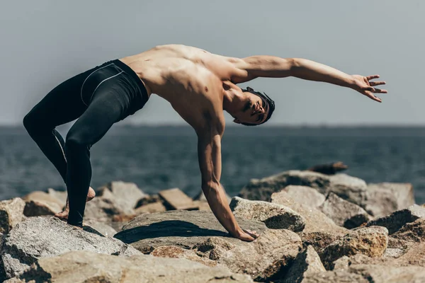 Handsome shirtless contemporary dancer on rocky coast — Stock Photo