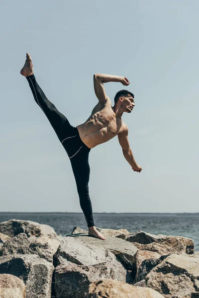Schöner hemdloser Mann tanzt auf felsigem Meeresufer — Stockfoto