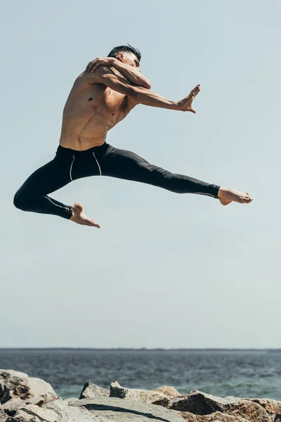 Hübsche, hemdlose Tänzerin springt über felsige Meeresküste — Stockfoto