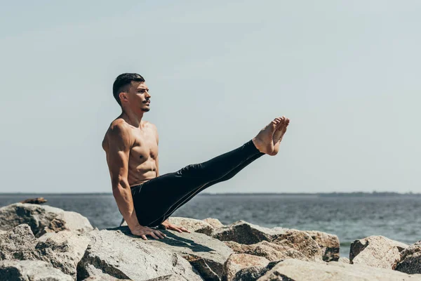 Athletic shirtless man doing arm balance on rocky seashore — Stock Photo