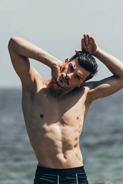 Bell'uomo senza camicia che si allunga il collo prima dell'allenamento davanti al mare — Foto stock