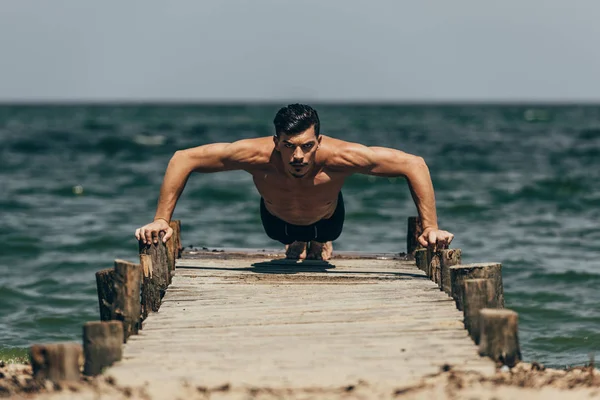 Bel homme athlétique faisant des pompes sur une jetée en bois — Photo de stock