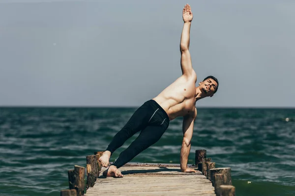 Sportlicher hemdsloser Mann macht Seitenplanke auf Holzsteg — Stockfoto