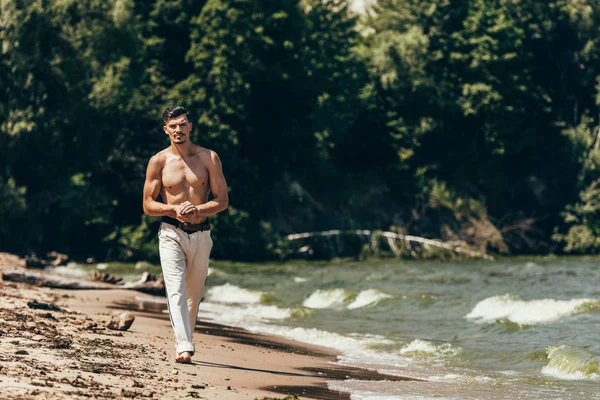 Atractivo hombre sin camisa caminando por la playa de arena - foto de stock