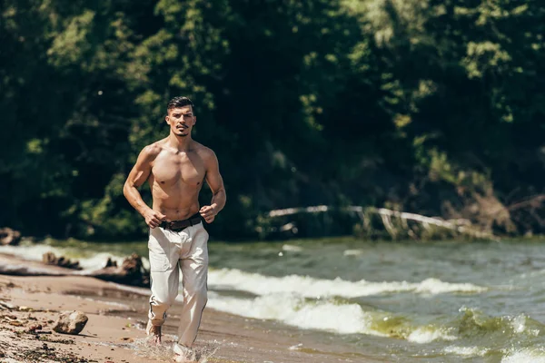 Attraente uomo senza maglietta jogging sulla spiaggia di sabbia — Foto stock