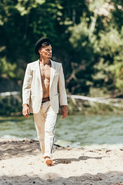 Schöner junger Mann in stylischem Anzug und Hut am Strand spazieren — Stockfoto