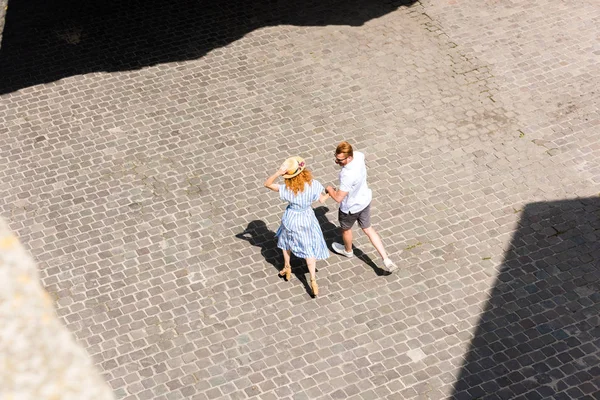 Високий кут зору рудої жінки в солом'яному капелюсі, що йде і тримає руку хлопця на вулиці міста — стокове фото