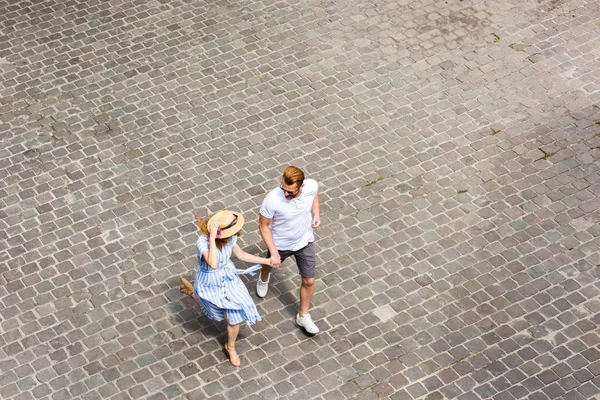 Vista ad alto angolo di donna in cappello di paglia a piedi con ragazzo rossa in strada città — Foto stock