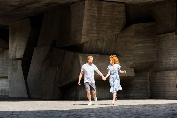 Happy redhead couple holding hands running at city street — Stock Photo