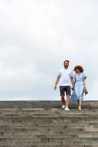 Low angle view of redhead couple holding hands and walking on stairs — Stock Photo