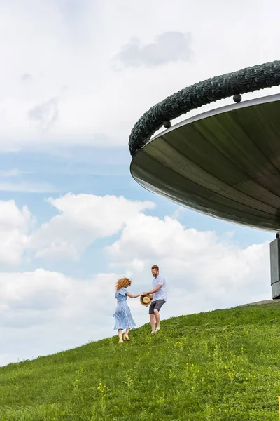 Vue lointaine du couple de rousses sur une colline herbeuse près d'un bâtiment moderne — Photo de stock