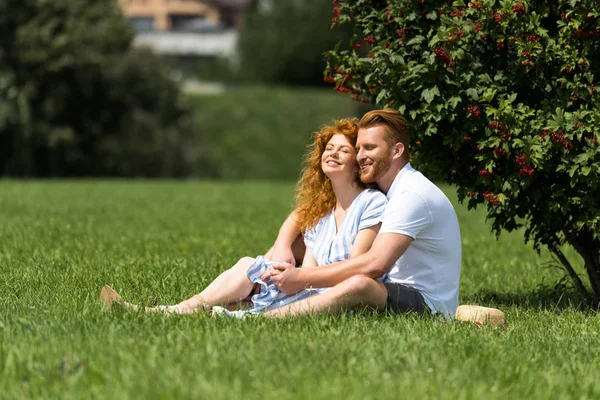 Sorridente rossa coppia seduta e divertirsi sull'erba nel parco — Foto stock