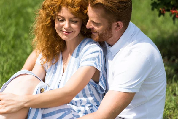 Щасливий рудий чоловік обіймає дівчину на траві на відкритому повітрі — стокове фото