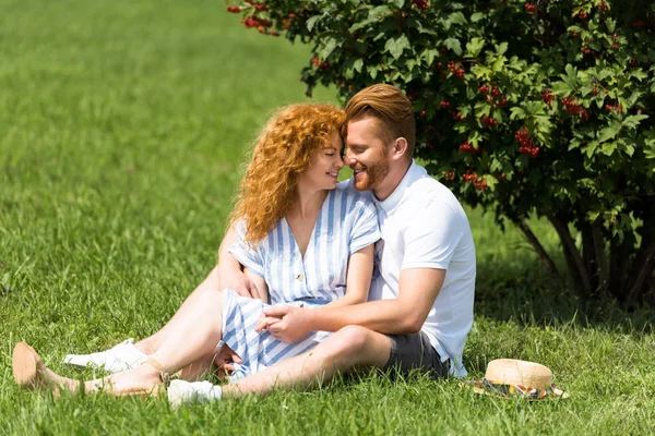 Sonriente pelirroja coupé sentado cara a cara en la hierba en el parque - foto de stock