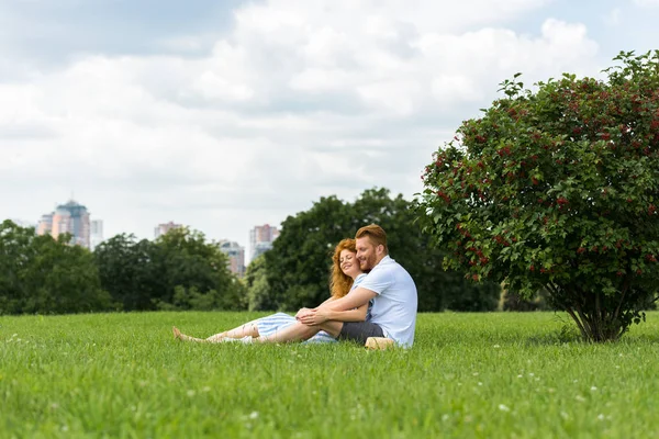 Vista distante do casal ruiva sentado na grama no parque — Fotografia de Stock