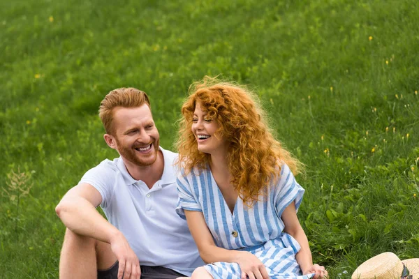 Riendo pelirroja mujer sentado con novio en herbáceo prado - foto de stock