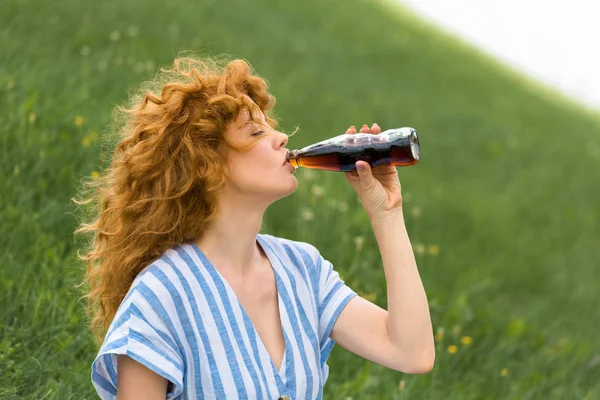 Side view of beautiful redhead woman drinking soda outdoors — Stock Photo